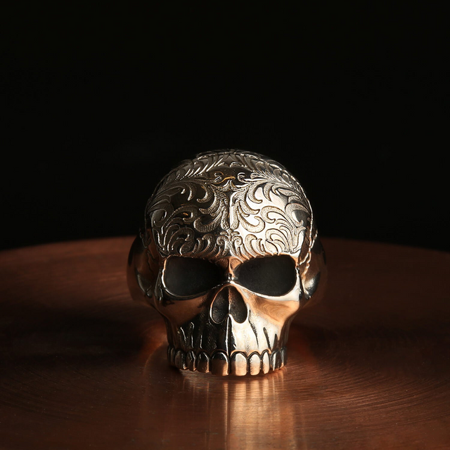 A skull ring with intricate patterns on a dark background.